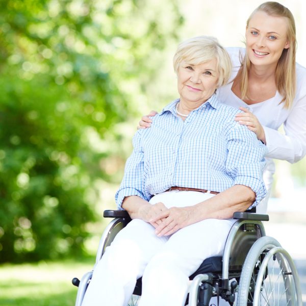 Walking out with patient Female caregiver and senior patient in a wheelchair looking at camera outside